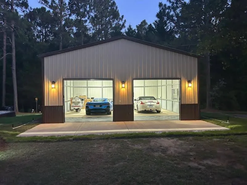 Illuminated two-bay steel garage at dusk with sports cars inside, built by METCO