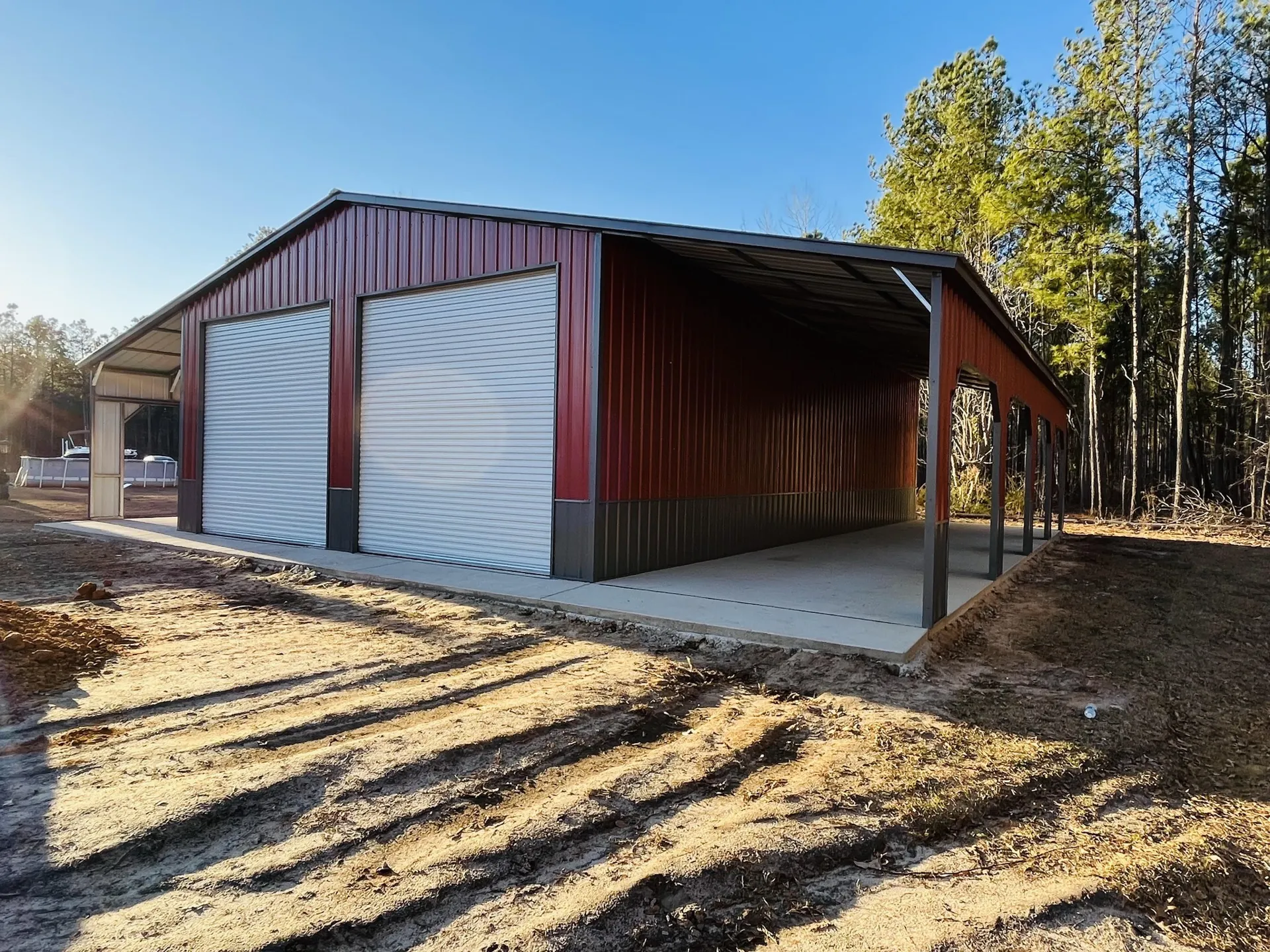 Red steel garage with attached open carport lean-to on a concrete pad, built by METCO